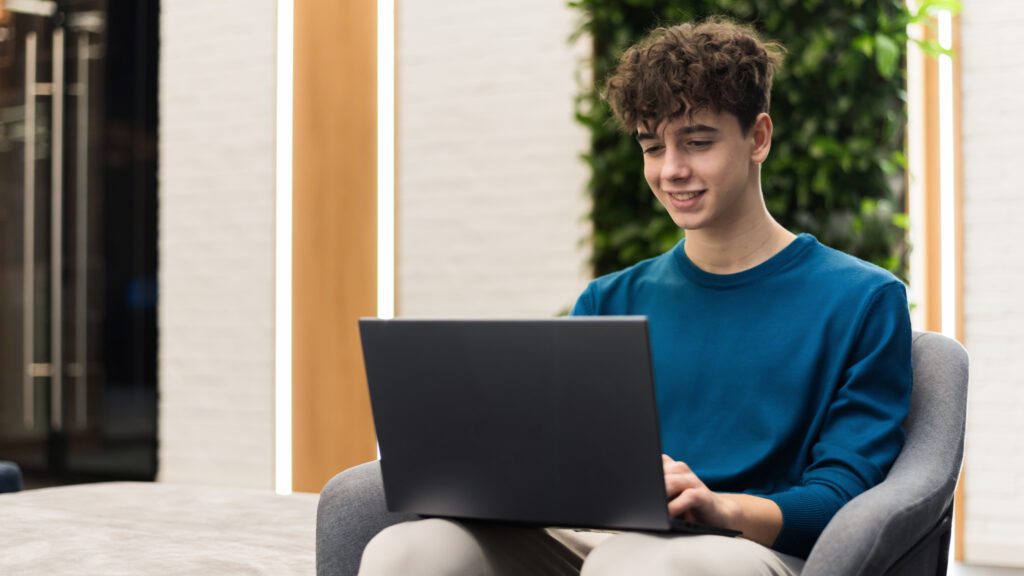 A young male student studying using a laptop while sitting in a chair at home